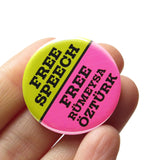 A round pinback button split half lime green & bright pink. Green half reads FREE SPEECH in black text. Pink half reads FREE Rumeysa Ozturk in black text. Button is held in a hand.