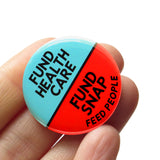 A round pinback button split between two colors, hospital scrubs green on the top and neon Advil red-orange on the bottom. The top of the button reads: FUND HEALTHCARE, The bottom reads: FUND SNAP, Feed People. Badge is held in a hand.