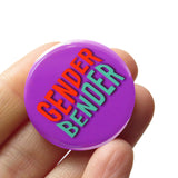 Round pinback button reading GENDER BENDER in Orange & light teal on a purple background. The button is held in a hand.