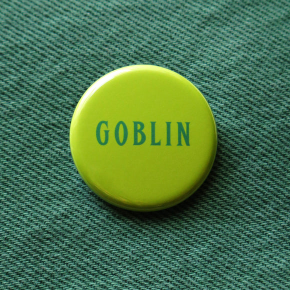 Round lime green pinback button that says GOBLIN in a narrow dark green font.  Button is on green denim.