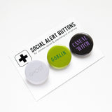 Three round pinback buttons lined up on a SOCIAL ALERT BUTTONS backing card. Reading left to right: GHOST in white & gray, GOBLIN in greens & CASUAL WITCH in black & lavender.  