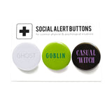 Three round pinback buttons lined up on a SOCIAL ALERT BUTTONS backing card. Reading left to right: GHOST in white & gray, GOBLIN in greens & CASUAL WITCH in black & lavender.  