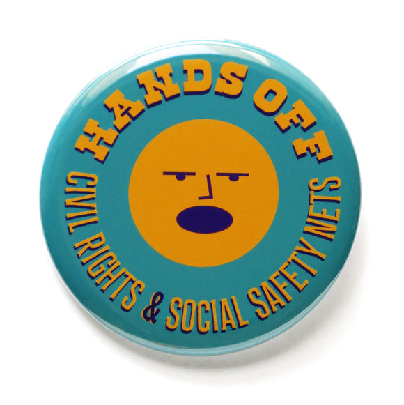 A round teal pinback button that reads HANDS OFF Civil Rights & Social Safety Nets yellow-orange text,  with an angry shouting face in the center of the button. 