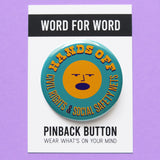 A round teal pinback button that reads HANDS OFF Civil Rights & Social Safety Nets yellow-orange text,  with an angry shouting face in the center of the button. Button is on a Word For Word branded backing card that reads Pinback Button, Wear What's On Your Mind