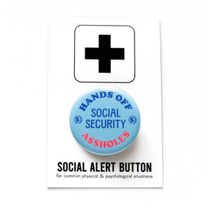 A round light blue pinback button with light dark blue text reads HANDS OFF SOCIAL SECURITY with two little illustrated coins with dollar signs on them, and A$$HOLES in neon red at the bottom. Button is held in a hand.