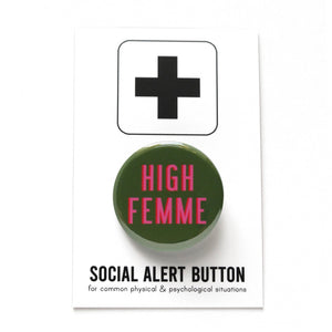 Round pinback button that HIGH FEMME. Pink text with a red shadow on an olive green background. Button is pinned to a Social Alert Button backing card
