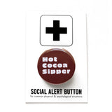 round chocolate brown colored 1..25" holiday themed pinback button that reads HOT COCOA SIPPER in a chunky white font. Button is on a Social Alert Button 