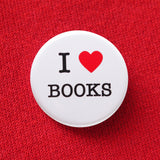A round white pinback button that reads I LOVE BOOKS, love being represented by a red heart. Button is pinned to a red sweatshirt.
