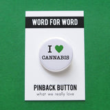 Round white button reads I LOVE CANNABIS. Green heart symbol represents love, remaining text is in black. Button is on a Word For Word branded backing card.