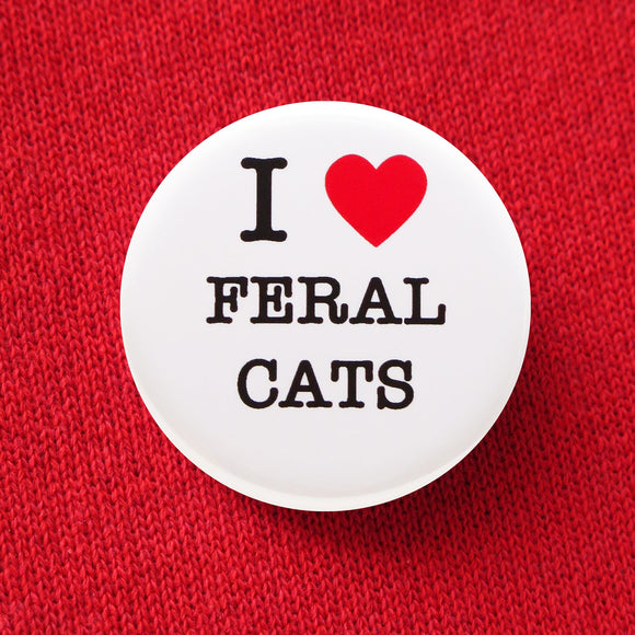 Round white pinback button that reads I Love Feral Cats. Love is represented by a red heart. Remaining text is in black font. Button is pinned to a red sweatshirt