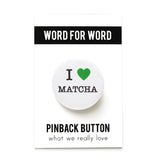 A round white pinback button that reads I LOVE MATCHA, has a green heart representing love, and the rest of the phrase is in a classic serif font. The button is attached to a backing card which reads the brand WORD FOR WORD on the top in a black bar, and PINBACK BUTTON on the bottom, What We Really Love as the tagline