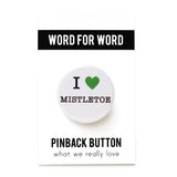 Round, white pinback button that says I LOVE MISTLETOE in classic black text with "love" being represented by a green heart. Button is on a WORD FOR WORD branded backing card.