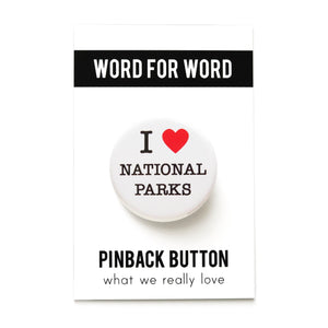 A round white pinback button that reads I LOVE BANNED NATIONAL PARKS. Love represented by a red heart. Button is pinned to a Word For Word What We Really Love branded backing card.