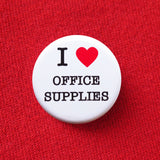 A round white pinback button that reads I LOVE OFFICE SUPPLIES, with love being indicated by a red heart. Button is pinned to a  red sweatshirt.