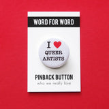 A round white pinback button that reads I LOVE QUEER ARTISTS in a black serif font, the love being indicated by a red heart. The button is on a white backing card that reads WORD FOR WORD in a black rectangle at the top, and reads Pinback Button, at the bottom of the card.