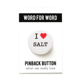 A round white button that reads I LOVE SALT. Love being represented by a red heart. Button is pinned to a Word For Word branded backing card.