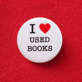 Round white pinback button that reads I LOVE USED BOOKS in 3 lines, with "love" being represented by a red heart illustration. Button is pinned to red sweatshirt