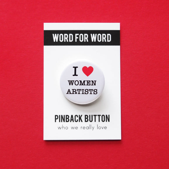 Round white pinback button that reads I LOVE WOMEN ARTISTS with a red heart indicating love. Button is on a Word For Word Pinback Button branded backing card.