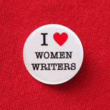 A round white pinback button that reads I LOVE WOMEN WRITERS with love being a red heart. Pinned to a red sweatshirt