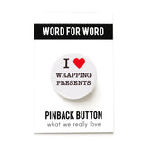 Round, white pinback button that says I LOVE WRAPPING PRESENTS in classic black text with "love" being represented by a red heart. Button is on a WORD FOR WORD branded backing card.