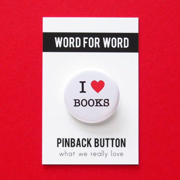 A round white pinback button that reads I LOVE BOOKS, love being represented by a red heart. Button is pinned to a Word For Word, What We Really Love branded backing card.