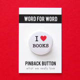 A round white pinback button that reads I LOVE BOOKS, love being represented by a red heart. Button is pinned to a Word For Word, What We Really Love branded backing card.