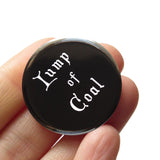 Black round pinback button that reads LUMP OF COAL in white old fashioned font. Badge held in a hand.