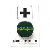 Round dark green button that reads MEDICATED in a neon green font. Badge is on a Social Alert Button backing card.