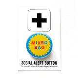 A round blue pinback button with a circular yellow starburst in the middle, and mixed color text that reads MIXED BAG. Button is pinned to a Social Alert Button backing card.