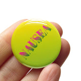 Round pinback button with yellow to green ombre background, with pink to green ombre text that reads NAUSEA in a wavy serif font. Button is held in a hand.