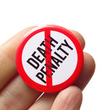 A round white button that reads NO DEATH PENALTY in black text with a red circle and slash to indicate being against the death penalty. Button is held in a hand.