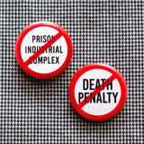 Two around white pinback buttons with a red circle & slash, one reading NO DEATH PENALTY, the other reads, NO PRISON INDUSTRIAL COMPLEX. Buttons are pined on a black & white tiny houndstooth print fabric.