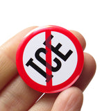 ICE in strong black text with a red circle and slash around it, to indicate being against ICE. Button is held in a hand.
