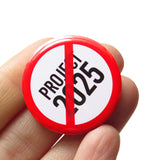 A round white button that reads NO PROJECT 2025 in black text with a red circle and slash to indicate being against billionaires. Button is held in a hand.