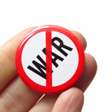 A round white 1.25" pinback button that reads WAR in solid black text with a red circle around it and a red slash through it, to indicate being against WAR, or Anti War. Button is held in a hand.