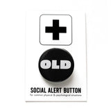 A round black pinback button that reads OLD in a chunky white font. The button is pinned to a Social Alert Button backing card.