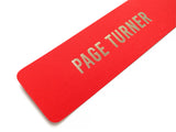 Close up of a vibrant red-orange vertical bookmark that reads PAGE TURNER in gunmetal silver foil embossed text.