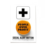 Round yellow-orange pinback button with black text that reads PEOPLE OVER PROFIT in an art deco font. Button is on a Social alert button backing card.
