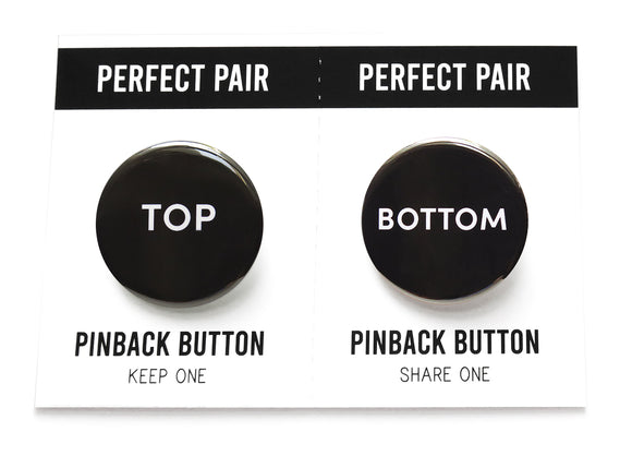 Two pinback buttons on a backing card with a center perforation to tear & share with a friend. Button the left reads TOP. Button on right reads BOTTOM. Both buttons are black with white text.