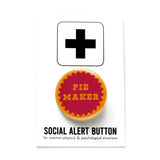 A round golden brown pie crust color 1.25" pinback button with a jammy berry center that reads PIE MAKER in golden cut out letter. Button is on a Social alert button backing card.