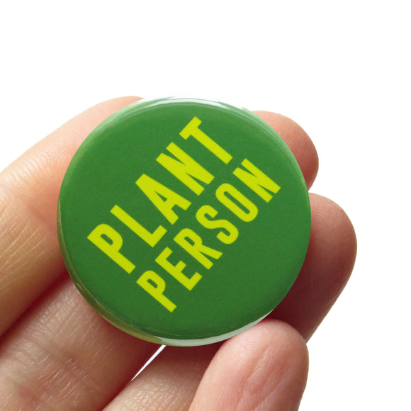 vivid medium green round pinback button, which reads PLANT PERSON in a neon green san serif  font. Button is held in a hand.