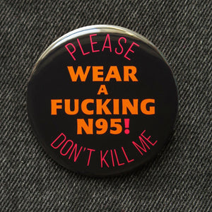 A round black pinback button that reads WEAR A FUCKING N95! in red text, in the center, and top & bottom curve orange text that reads PLEASE DON'T KILL ME. 