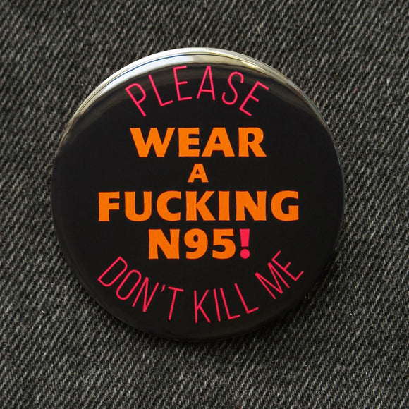 A round black pinback button that reads WEAR A FUCKING N95! in red text, in the center, and top & bottom curve orange text that reads PLEASE DON'T KILL ME. 