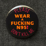A round black pinback button that reads WEAR A FUCKING N95! in red text, in the center, and top & bottom curve orange text that reads PLEASE DON'T KILL ME. 