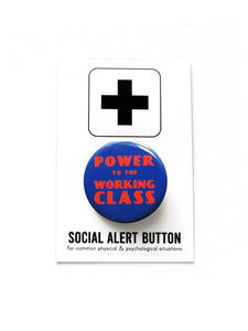 Round blue pinback button with red-orange text that reads POWER TO THE WORKING CLASS in an art deco font. Button is held in a hand.