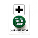 A round hunter green 1.25" pinback button that reads PROTECT PUBLIC LANDS in a white fonts. Button is on a Social Alert Button backing card.