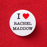 Round white pinback button that reads I LOVE RACHEL MADDOW, with love being represented by a red heart. Button is pinned to a red sweatshirt