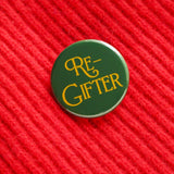 Rich green round pinback button that reads RE-GIFTER in decorative golden yellow font. Button is on a bright red soft sweater with a diagonal rib pattern.