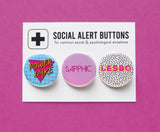 Three round pinback buttons in various vintage 1980's styles on a SOCIAL ALERT BUTTONS backing card. Buttons Left to Right: A blue button with a magenta triangle and gold text that reads POWER DYKE, A pink ombre button that reads SAPPHIC in a thin magenta pink font & a white button with tiny Memphis style black squiggles that reads LESBO in pink text with a Yellow drop shadow.