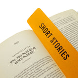 A rich marigold yellow  vertical bookmark that reads SHORT STORIES in gunmetal silver foil embossed text, marking the start of the 1967 Raymond Carver short story, Will you please be quiet, please?